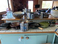 Wide view of the kitchen counter displaying various pots, pans, mixing bowls, glass containers, double boiler and wok.