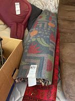 Two rugs rolled and stacked, one with a multicolor geometric and floral pattern, the other red with traditional design.