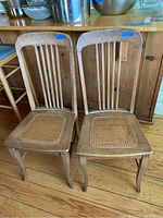 Two vintage wooden chairs side by side, showing full front view including cane seats and vertical slat backs.