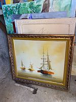 Framed painting depicting three sailing ships on water with warm tones and a decorative frame.