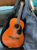 Full view of Yamaha classical guitar lying inside a black padded guitar case with case open.