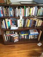Full view of wooden bookshelf filled with books on four shelves. Books are various novels and older books.