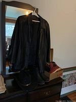 Danier black leather jacket hanging on a white plastic hanger in front of a mirror; next to the jacket are two pairs of boots and a black felt Western hat on a dark dresser.