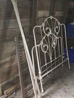 Overview of antique cast iron bed components including headboard, footboard, side rails, and spring in a dimly lit room.
