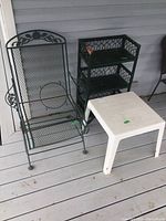 Photo showing black metal deck spring chair, green wooden shelf with three tiers, and white resin table on porch deck