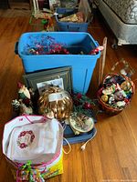 Blue bin and assorted Christmas statuettes including Santa, with framed print and basket of ornaments on wooden floor