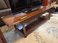 Full view of rectangular wooden coffee table with a flat top, a lower shelf, and turned legs. Top surface holds a TV and shows signs of wear.