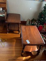Two wooden end tables with turned legs and lower shelves, placed on a wood floor near holiday decorations. Visible wear on tabletops.