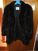 Full view of dark brown Woodleys fur coat on hanger, showing front and interior lining.