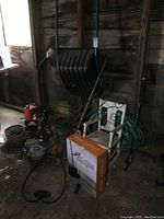 Wide view showing snow scoop shovel with blue handles, vintage child's rocker, garden hose, garden tools, chain, fishing pole, and hedge trimmer in shed.