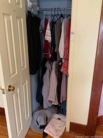 Photo showing closet with assorted ladies clothing including tops, jackets, a grey hat, and clothing hanging on hangers.