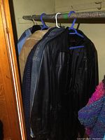Five coats hanging on a rod: faux suede tan coat, denim jacket, Danier black leather coat, long wool coat, down-filled ski jacket.