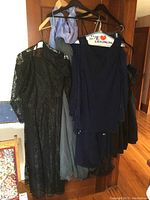 Five ladies formal dresses hanging on a door, varying in style and color including black lace and light blue chiffon