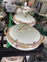 Two Limoges porcelain tureens with lids, floral pattern borders with gold accents and handles. One tureen has a broken handle visible.
