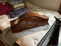 Vintage wooden mantel clock on bed, showing full length and curved top profile.