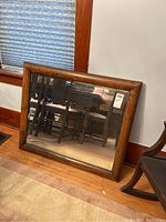 Front view of beveled glass mirror with medium-tone wooden frame, showing full reflection and general condition.