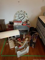 Full view of printer box, clock, office supplies, cables, desk lamp and other items arranged near bed and side table