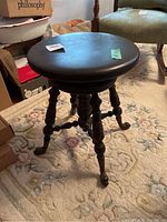 Full view of the piano stool showing the round seat, turned legs, and claw feet on floral carpet.