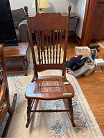 Front view of wooden rocking chair showing decorative carved back and caned seat with damage.