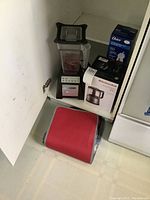 Blendtec blender, KitchenAid mini food processor box, Oster hand blender box on shelf, Wolfgang Puck garnishing set in red case on floor