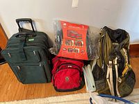 Full lot overview showing green suitcase, red backpack, green backpack with steel frame, packing cubes in packaging, and white storage bags/folders.