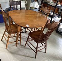 Photo of solid wood drop leaf dining table and four mismatched wooden chairs showing overall condition and design.