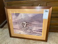 Full view of the framed art print depicting a horse-drawn carriage on a country road with hills in the background. The art is behind glass in a wooden frame with a beige mat.