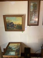 Four framed landscape paintings on wall and floor, showing rustic and natural scenes with visible signed marks on paintings.