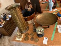 Overview of the brass items and other lot components on a table, showing umbrella stand, bowl, bucket, coins, snow globe, Empire State Building, and pharaoh statue.