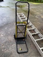 Front view of convertible dolly hand truck showing black and yellow metal frame and diamond plate extended base.