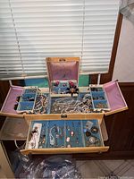 Open wooden jewelry box displaying multiple compartments with necklaces, pendants, brooches and earrings