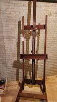 Full view of the standing wooden easel against a brick wall showing the entire frame and base.