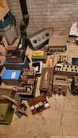 Wide view of the basement floor with an assortment of vintage electronic testing equipment, solder set, and hand tools arranged closely together.