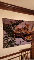 Full view of the hooked rug hung on a wall showing the leopard and cub reclining in a tree with surrounding foliage.