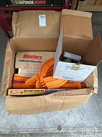 Overhead view of open cardboard box showing orange plastic Hot Wheels track pieces and a box labeled Sizzlers California 8 Race Set inside