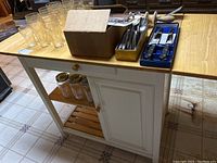 Kitchen island with butcher block wooden top and two folding side leaves. White painted base with drawer and cabinet door, wooden knobs. Items on and inside not included.