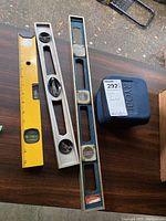 All four levels pictured on dark wood surface including Ryobi laser level in blue case and three straight levels of different lengths and materials.