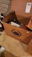 Photo showing a cardboard box labeled 'Coast' containing leathercraft tools and materials, including metal stamps and leather straps.