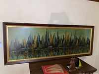 Full view of framed city skyline painting showing the entire horizontal composition and wooden frame.
