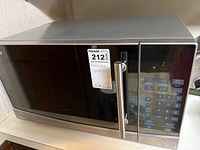 Front view of Oster microwave with reflective black door and stainless steel handle, showing some wear.