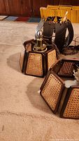 Two pendant lights with woven cane side panels and brass fittings on a beige carpet floor. Showcasing the exterior design and condition.