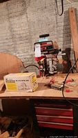 Craftsman 10-inch radial saw with stand and boxed mitre box on wooden bench in basement workshop.
