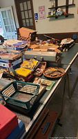 Image showing a wide view of the garage table with an assortment of tools, toolboxes, boxes with smaller tools and accessories scattered on plywood board and green table.