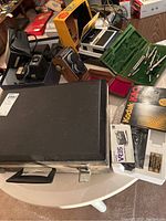View of the lot on round table showing multiple vintage cameras, Kodak K80 box, drafting tools in green case, black carrying case, and some packaging.