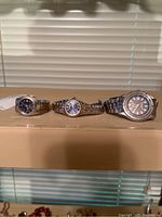 Four men's wristwatches arranged in a row on a surface showing different dial colors and metal bands