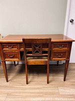 Front view showing the full desk with four drawers and a matching chair with a decorative back.
