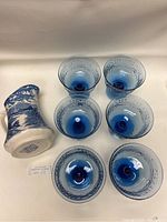 Top-down view of the ceramic jug and six blue glass dessert bowls clearly showing the blue and white pattern on the jug and the blue glass with textured rims on the bowls.