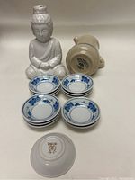 Full set of one Mini Buddha pitcher and eight sauce dishes arranged for display on a neutral surface.