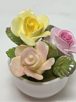 Close-up of three rose flowers in yellow, pink, and light pink with green leaves on a white rounded base.