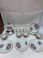 Full view of tea cups, saucers, and bread & butter plates with floral design and gold trim.